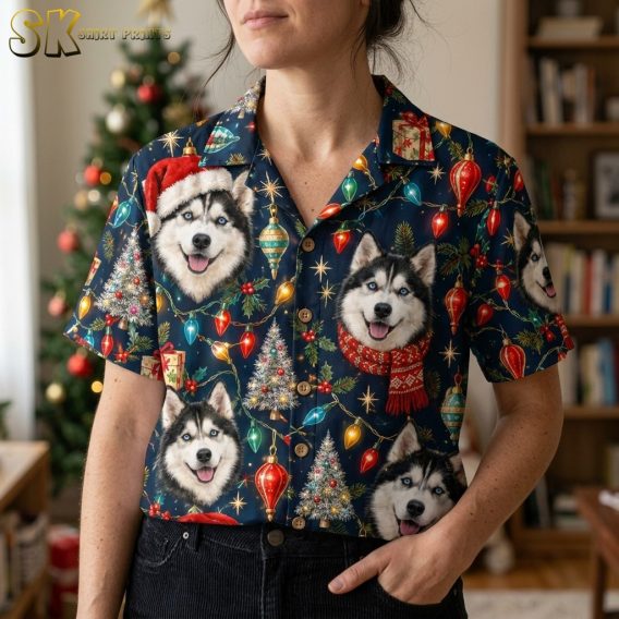 A woman wearing the navy husky shirt stands in a home interior near a Christmas tree, with the camera close enough to show individual husky faces — one in a Santa hat, one in a red scarf — alongside glowing string lights and ornament motifs.