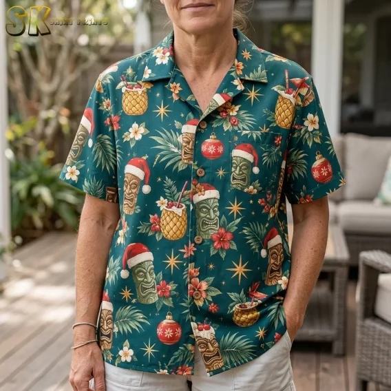 An older woman stands on a wooden porch wearing a christmas hawaiian shirt womens style, the close-up framing showing tiki faces with Santa hats, red ornaments, and golden starbursts across the front.