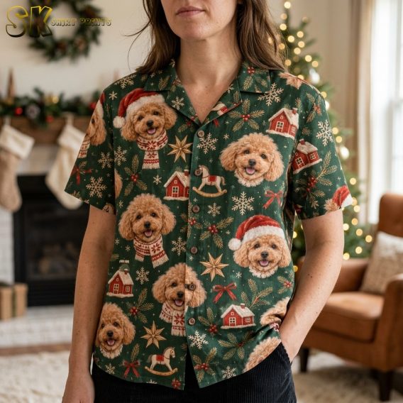A woman wearing xmas hawaiian shirts styled with a camp collar stands near a glowing Christmas tree, showing the dense pattern of poodle faces, gold stars, red bows, and pine sprigs up close.