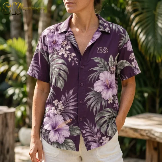 A woman photographed from the chest up outdoors wears a purple floral button-up shirt, with the 'YOUR LOGO' text printed clearly on the upper left chest amid hibiscus and palm-leaf motifs.