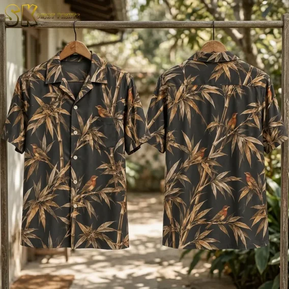 Front and back of the bird-and-bamboo shirt hang from wooden hangers on a rack outdoors, with leafy plants behind them.
